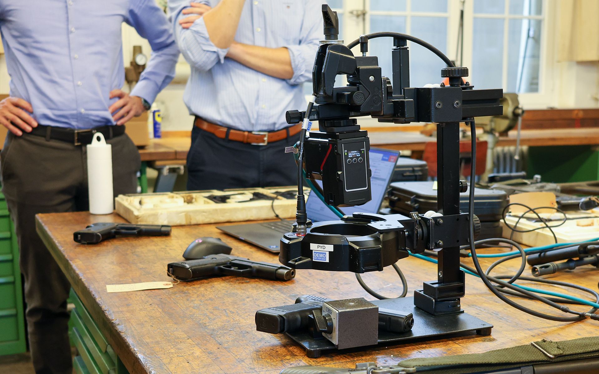 In the centre, we see the system for automatic scanning of weapon serial numbers on a table with rifles and pistols.