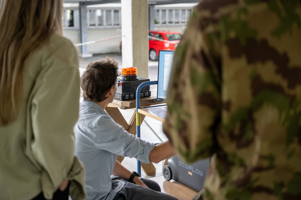 Une personne travaille sur un poste de simulation équipé de plusieurs écrans, tandis que d’autres parti-cipants suivent l’instruction.