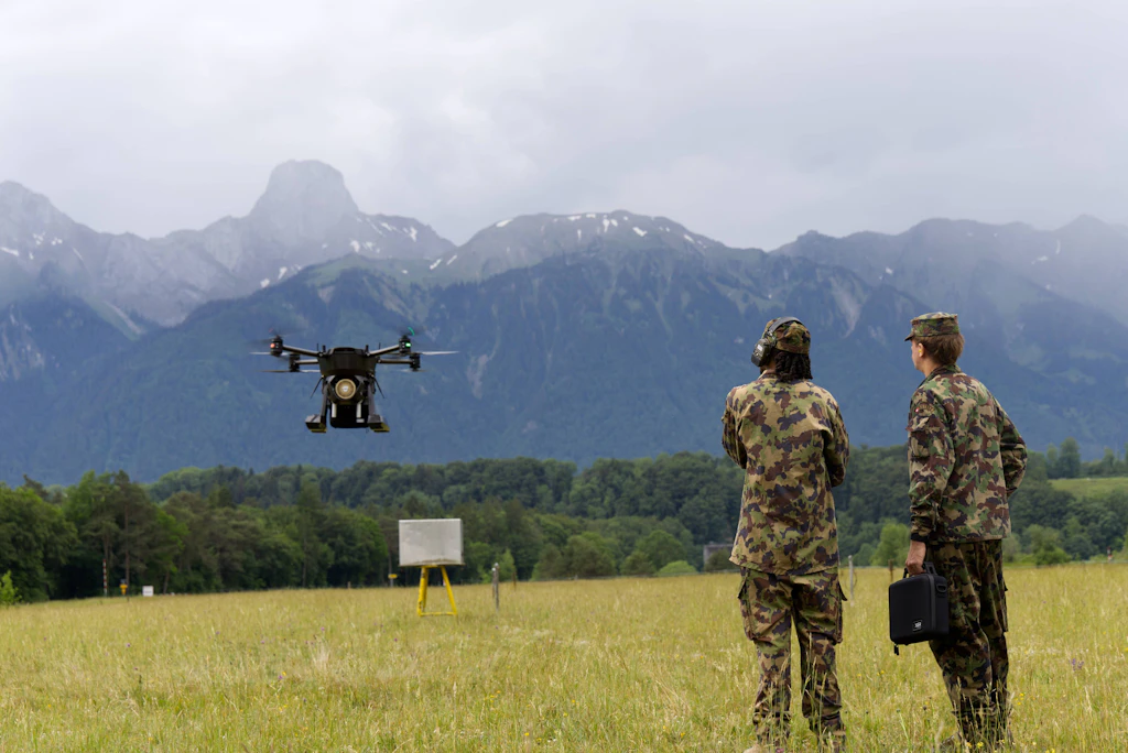Due militari osservano un drone da trasporto durante un volo di prova in un campo di addestramento.